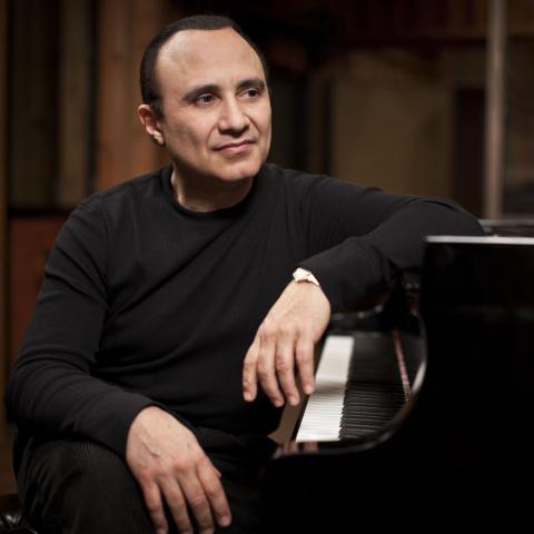 Michel Camilo sits at a piano 