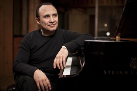 Michel Camilo sits at a piano 