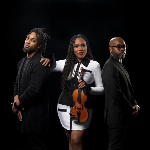 Chelsey Green poses against a black background holding a violin with the two members of her band the Green Project standing to either sideroject