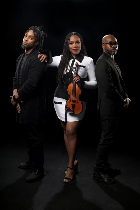 Chelsey Green poses against a black background holding a violin with the two members of her band the Green Project standing to either sideroject
