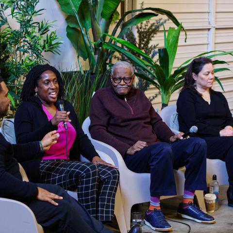 Five adult panelists sit in white chairs facing an audience (not pictured)