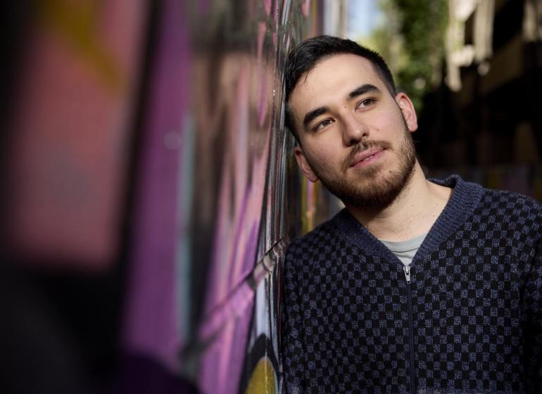 a young dark haired man leaning against a building wall