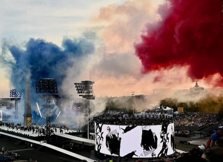 Aerial shot of the 2024 Paralympics opening ceremony featuring a stage of performers and a plume of smoke in the colors of the French flag