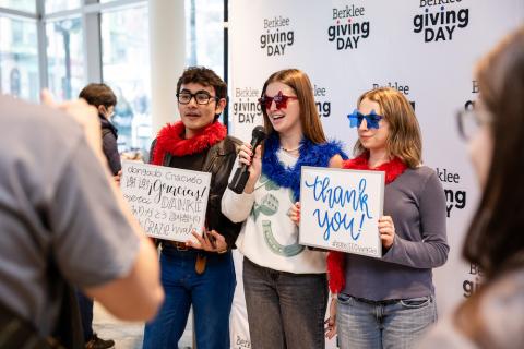 Students smile together in front of the Giving Day step-and-repeat while holding "thank you" signs