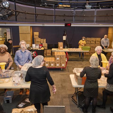 Faculty and staff wearing hair nets work at tables preparing food at a volunteer event