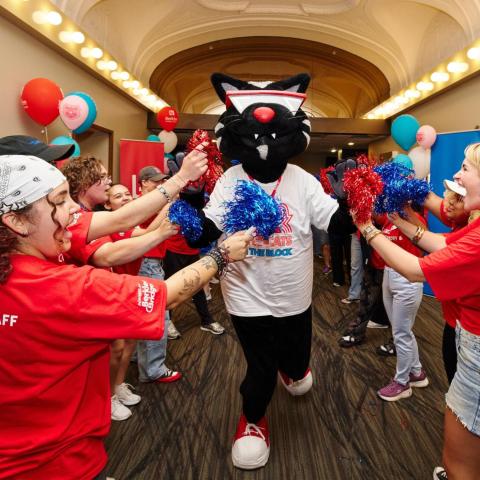 people wearing red t-shirts flank Mingus the Cat in Berklee Performance Center lobby.