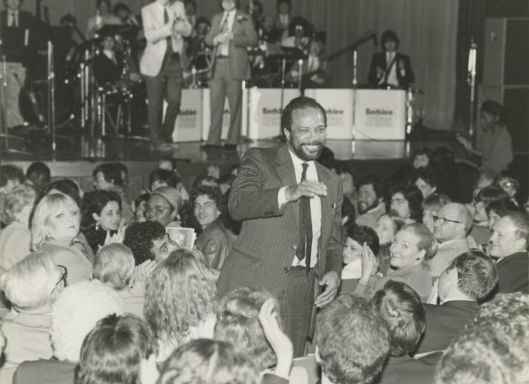 Quincy Jones standing amidst a seated crowd at Berklee commencement in 1983