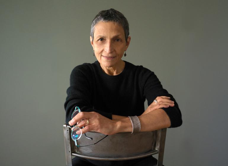 Composer and Boston Conservatory professor Laura Kaminsky posing in a black shirt, sitting on a chair backwards.