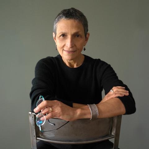 Composer and Boston Conservatory professor Laura Kaminsky posing in a black shirt, sitting on a chair backwards.