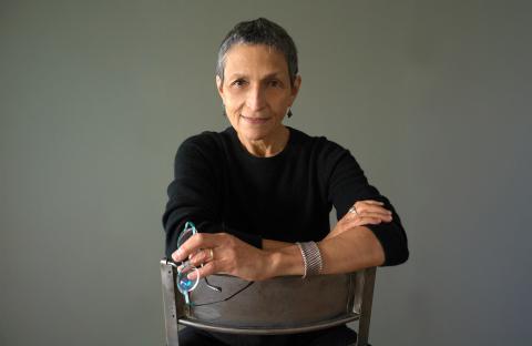 Composer and Boston Conservatory professor Laura Kaminsky posing in a black shirt, sitting on a chair backwards.