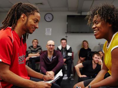Two seated students rehearsing a scene in front of their classmates and teacher