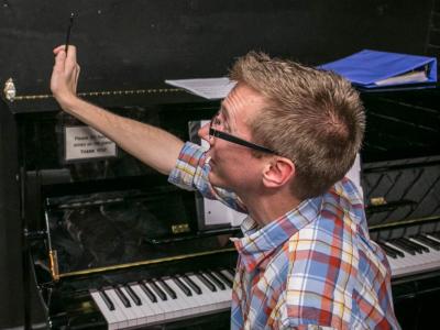 Person sitting in front of piano, talking to someone out of frame