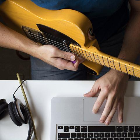 Student holding a guitar and working on a computer