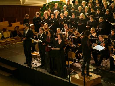 four vocalists singing in front of a choir and string section
