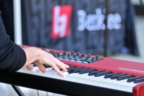 Student playing keyboard in front of berklee banner
