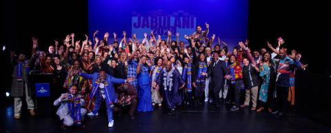 A crowd of students celebrates on stage with a blue backdrop that says Jabulani
