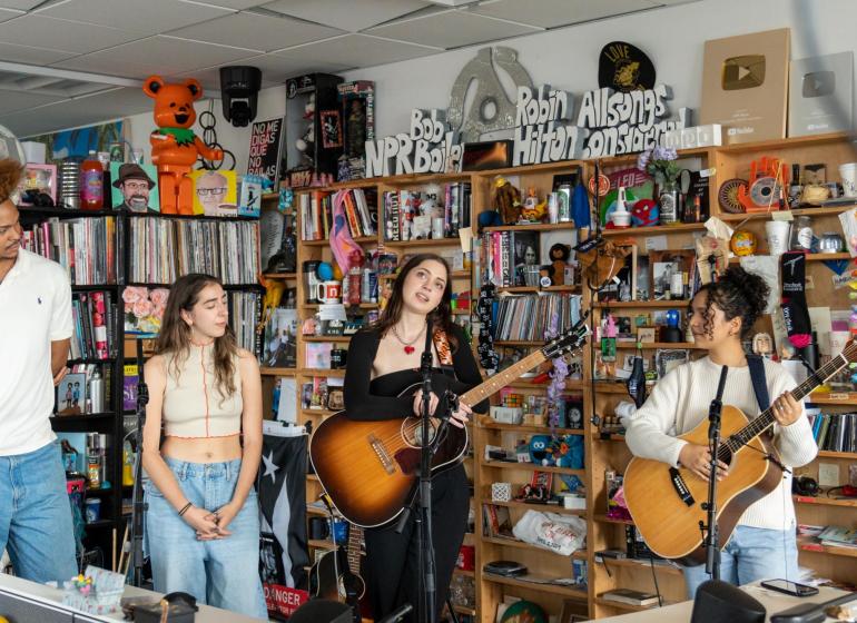 four musicians perform in an office in front of bookshelves