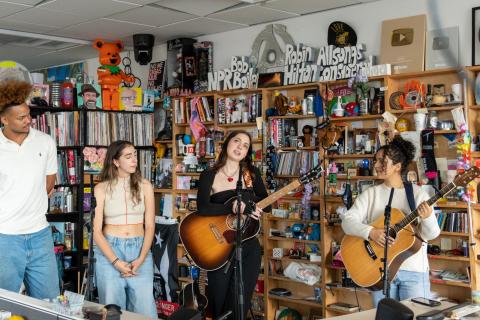 four musicians perform in an office in front of bookshelves