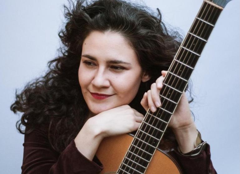 Mercedes Escobar leaning on an acoustic guitar 