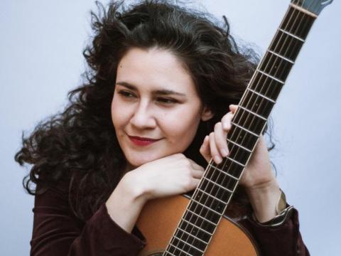 Mercedes Escobar leaning on an acoustic guitar 