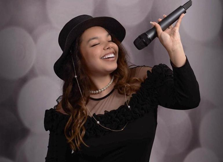 Formal portrait of Paris Pineyro with her eyes closed and holding a microphone above her head