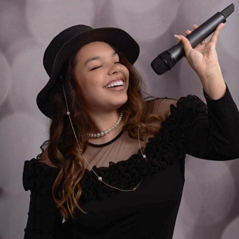 Formal portrait of Paris Pineyro with her eyes closed and holding a microphone above her head