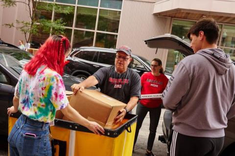 a picture of a family putting items into a bin from their car on move in day