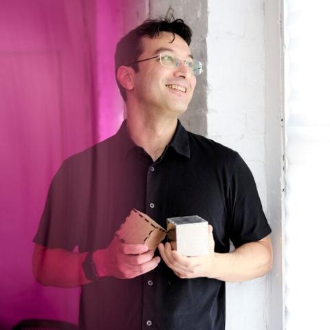 picture of akito van troyer holding two small custom-built musical cubes