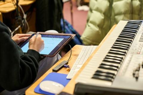 A person's hands writing on a digital tablet next to a MIDI keyboard workstation