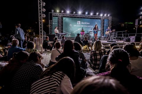 A concert at Berklee Valencia showing people in the crowd sitting and watching a band perform at night. 