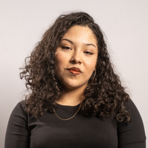 Student with olive skin and black curly hair smiles against a white background.