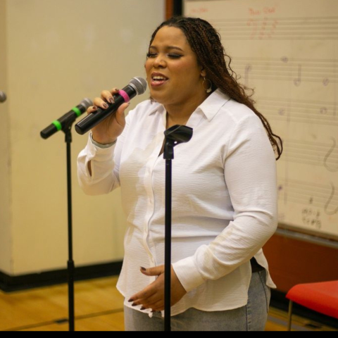 Student sings into microphone at Stax Music Academy wearing a white dress shirt and golden braids.