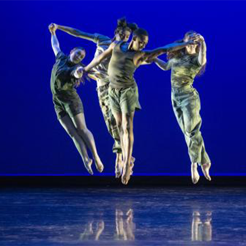 Three dancers leaping upward in front of a blue background