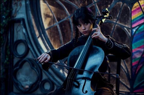 Jenna Ortega as Wednesday seated and playing a cello in her spooky dorm room